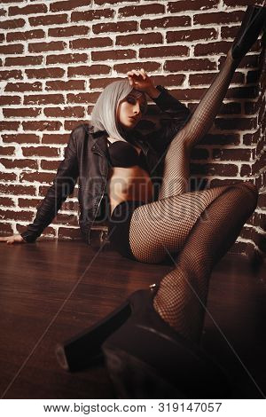 Girl In Net Tights And A Leather Jacket With Long Legs In The Interior Loft Studio. Girl In A Bra In