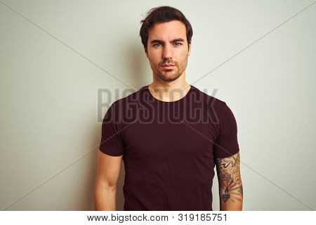 Young handsome man with tattoo wearing purple casual t-shirt over isolated white background Relaxed with serious expression on face. Simple and natural looking at the camera.