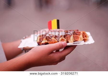 Hand Of A Girl Holding A Chocolate Waffle With Brussels Flag In A Street Of Ghent