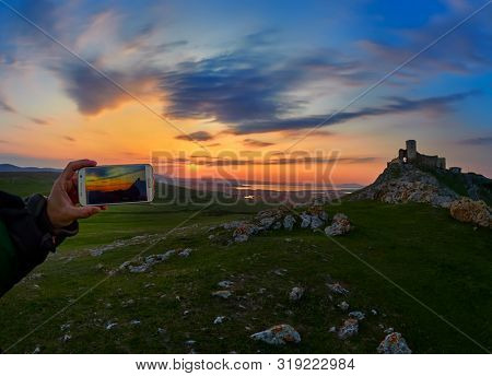 Enisala fortress at sunset, Dobrogea, Romania - man taking photo with the phone