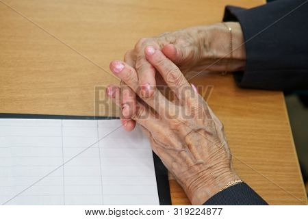 Hands Of An Elderly Woman Sitting At A Table Suffering From Stratification Of Nails. Social Problems