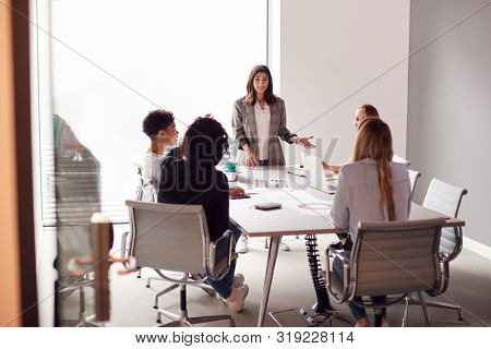 Female Boss Gives Presentation To Team Of Young Businesswomen Meeting Around Table In Modern Office