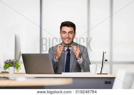 Handsome Caucasian Businessman Holding A Pen In His Hands, On A Table With A Notebook And A Coffee M