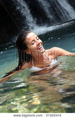 Beautiful woman enjoying bathing near natural waterfall