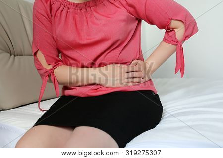 Woman Suffering From Pain In The Side. Slim Girl Sitting On Bed At Home With Hands On Left Side, Con