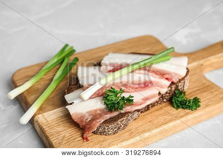 Board With Pork Fatback Sandwich And Onions On Grey Stone Background