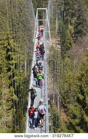 Bad Wildbad, Germany - April 22, 2019: Tourists Walk Along A Long And Suspended Iron Cable Bridge Fo