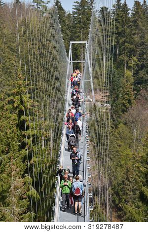 Bad Wildbad, Germany - April 22, 2019: Tourists Walk Along A Long And Suspended Iron Cable Bridge Fo