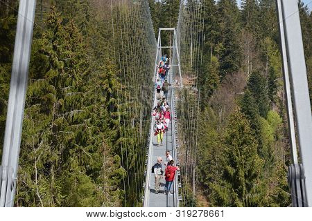 Bad Wildbad, Germany - April 22, 2019: Tourists Walk Along A Long And Suspended Iron Cable Bridge Fo