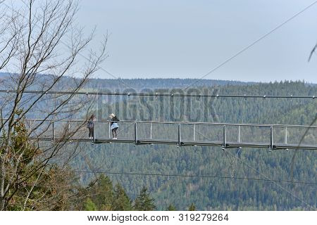 Bad Wildbad, Germany - April 22, 2019: Tourists Walk Along A Long And Suspended Iron Cable Bridge Fo