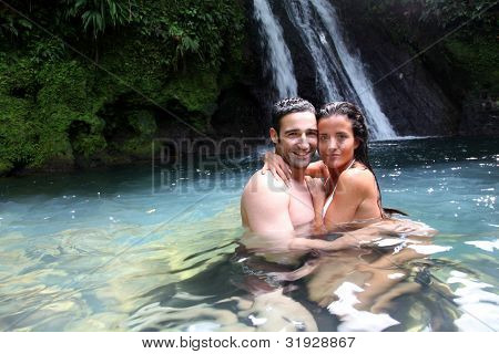 Happy couple bathing near waterfall in island