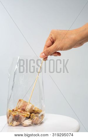 Woman's Right Hand Using Skewer Pick Up  Grilled Banana From Plastic Bag On Grey Background, Close U