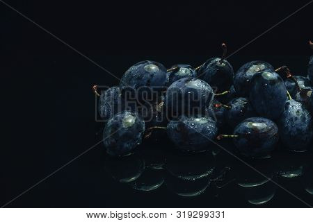Beautiful Fresh Blue Pulms On A Black Glass Table And Dark Background.