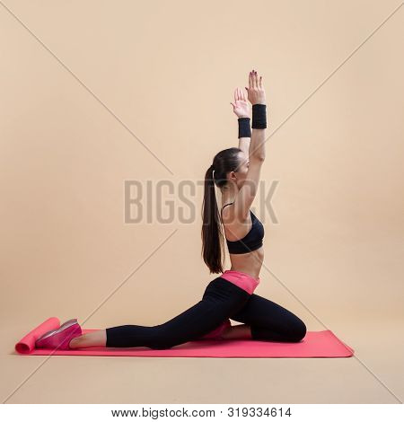 Young Attractive Girl With A Ponytail, Brunette, Sitting In The Pose Of A Pigeon With His Hands On A