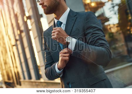 Stylish Man. Confident Businessman In Full Suit Adjusting His Sleeve While Standing Outdoors