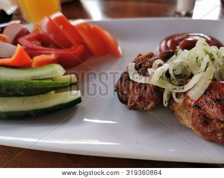 Barbecue, Pieces Of Pork Cooked On Coals And Sliced Vegetables - Cucumbers, Tomatoes, Salad On A Whi