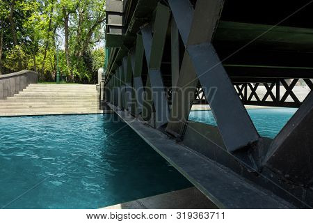 Bridge Across Water Channel. Metal Frame Structure Over Pure Calm River. Modern Urban City Landscape