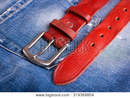 Red Leather Belt And Blue Jeans Close-up. A Belt Lying On Denim. Fashionable Red Belt Close-up.