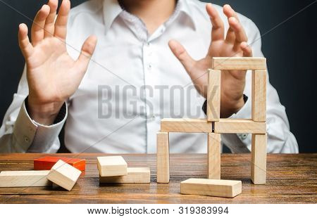 The Man Looks Frightened At The Collapse Of The Constructed Structure. Concept Of Mistakes And Failu
