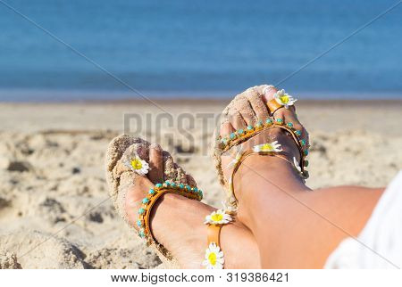 Holidays At Sea Background With Copy Space. Female Feet Shod In Sandals Lay On Golden Sand Near Seas