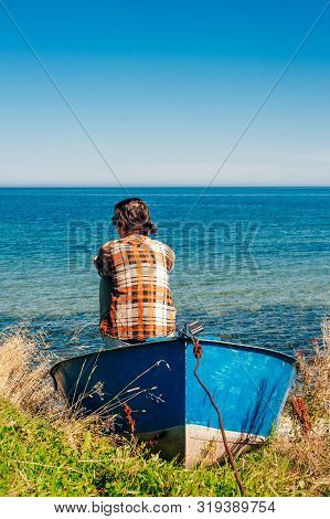Back View Of A Woman Sitting On Fishing Boat In A Calm Lake Water.