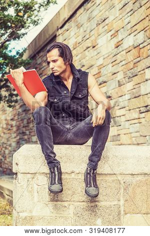Young Modern East Indian American Man Wearing Black Sleeveless Jacket, Jeans, Sneakers, Sitting On S
