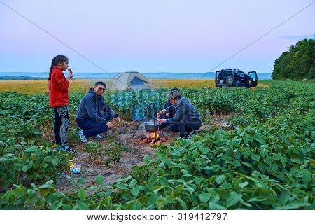 Family traveling and camping, twilight, cooking on the fire. Beautiful nature - field, forest and moon.