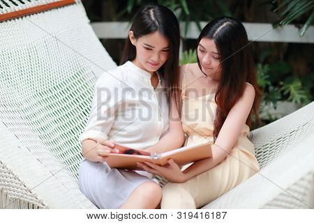 Young And Cute Asian Women Lying In A Hammock And Looking Photo Album During Holiday