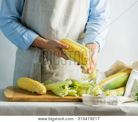 A Female Cook A Cotton Apron Cleans Ripe Corn On The Cob. Rustic Natural Style. The Concept Organic 
