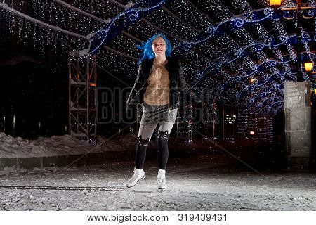 Girl With Blut Hair Skating On The Ice Arena In The Evening City Square In Winter