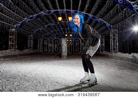 Girl With Blut Hair Skating On The Ice Arena In The Evening City Square In Winter