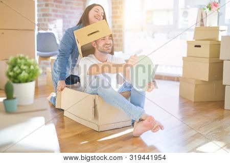 Funny and crazy couple having fun riding a cardboad box as a car, smiling happy and lauging at new home