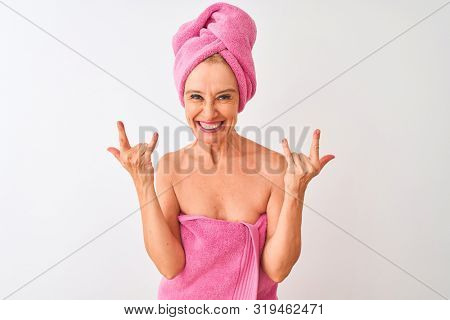 Middle age woman wearing shower towel after bath standing over isolated white background shouting with crazy expression doing rock symbol with hands up. Music star. Heavy concept.