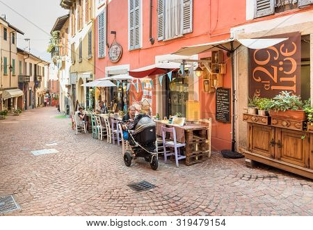 People Enjoying The Typical Italian Street Bars And Restaurants In The Historic Center Of Luino, Ita