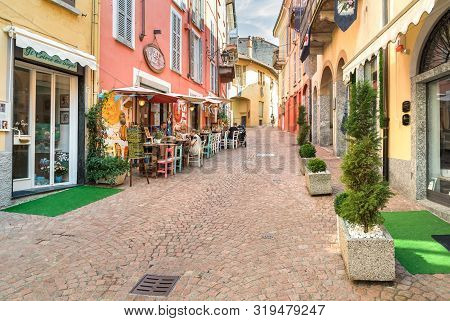 People Enjoying The Typical Italian Street Bars And Restaurants In The Historic Center Of Luino, Ita
