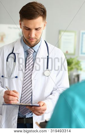 Portrait Of Physician Looking Down At Notepad Overwhelmed With Concerns. Man Wearing White Robe, Ste