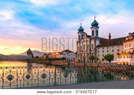 Jesuit Church And Water Tower, Wasserturm Along The River Reuss At Sunrise In Old Town Of Lucerne, S