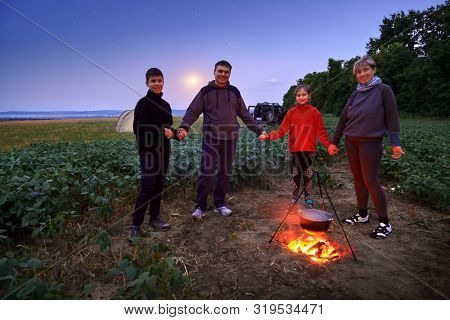 Family traveling and camping, twilight, cooking on the fire. Beautiful nature - field, forest, stars and moon.