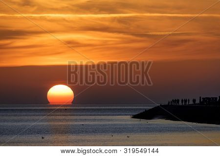Sunset In The North Sea In Germany, Tourists As Silhouettes On The Shore Enjoy The Dramatic Red Sky,
