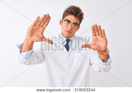 Young handsome sciencist man wearing glasses and coat over isolated white background doing frame using hands palms and fingers, camera perspective