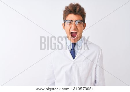 Young handsome sciencist man wearing glasses and coat over isolated white background angry and mad screaming frustrated and furious, shouting with anger. Rage and aggressive concept.