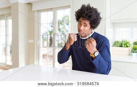 Young african american man wearing casual sweater sitting at home Ready to fight with fist defense gesture, angry and upset face, afraid of problem