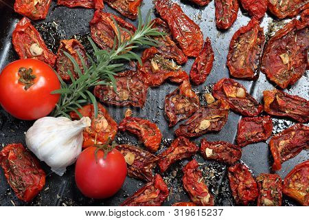 Sun-dried Tomatoes With Spices And Garlic On A Baking Sheet. Nearby Are Fresh Rosemary, Tomatoes And