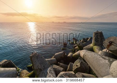 Beautiful Sunset Seascape. Breakwaters Tetrapods Ashore Of Pier. Cargo Ships On The Horizon. Travel 