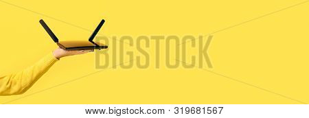Black Wifi Router On Hand Over Yellow Background, Panoramic Mock Up Image