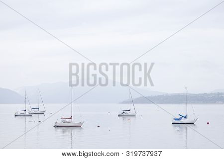 Boats Resting In Calm Tranquil Water Surround By Mountains In Scottish Landscape