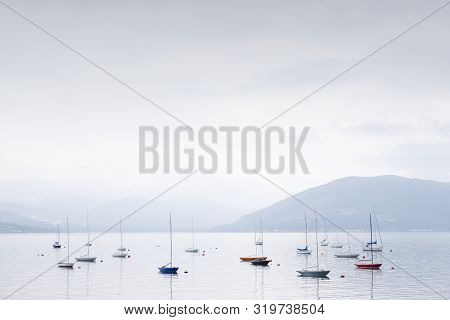 Boats Resting In Calm Tranquil Water Surround By Mountains In Scottish Landscape