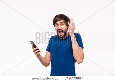 Pretty Brunet Man In A Blue Shirt With Beard And Mostaches Shocked Holding Smartphone Looking At The