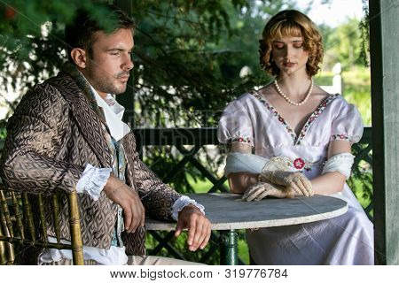 Handsome Young Couple In Vintage Clothing Sit In Gazebo Deep In Thought.