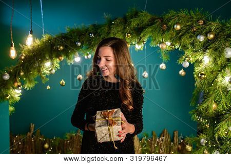 Girl With A Gift On The Background Of Christmas Decoration. Happy Woman With Gift Box In Christmas D